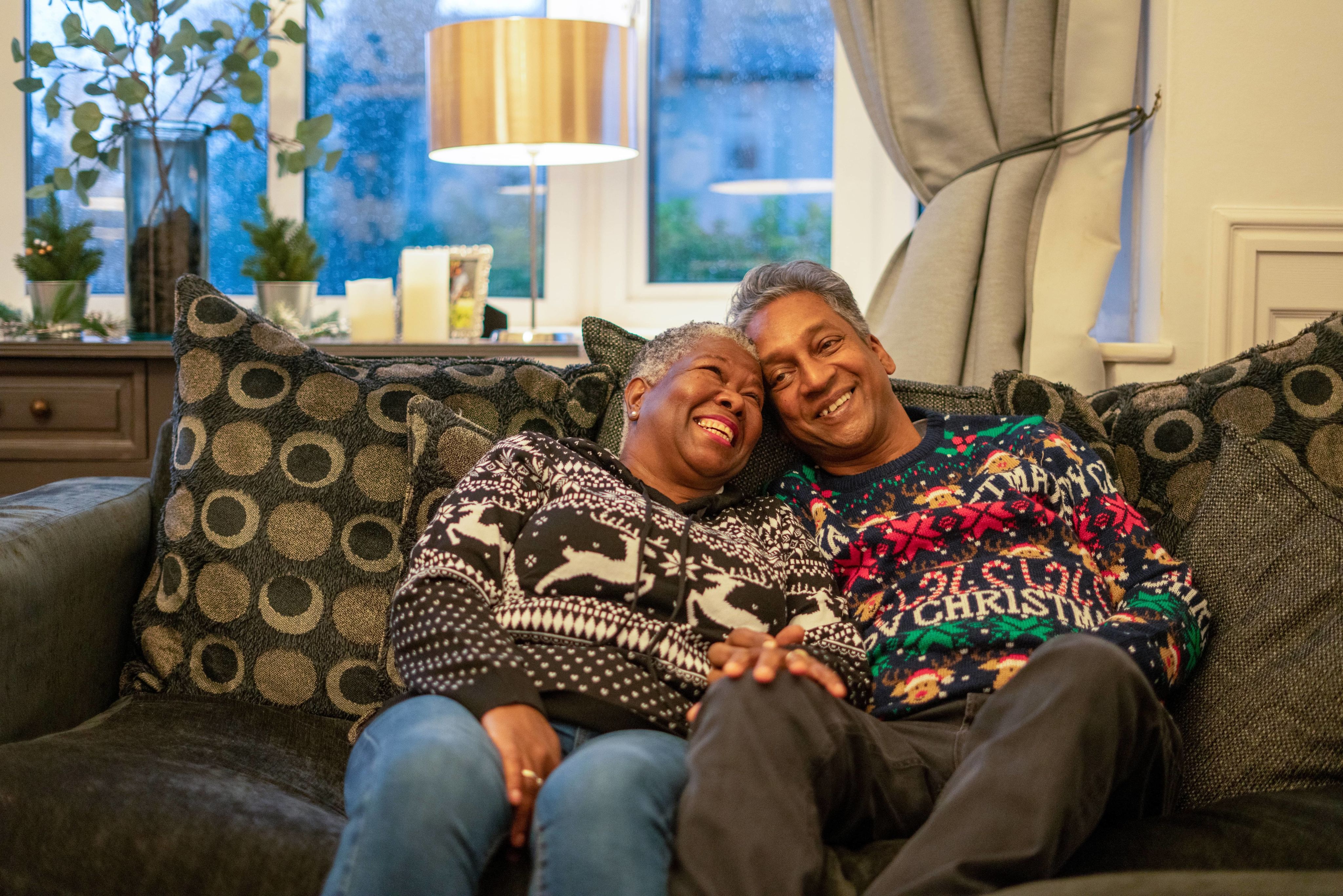 Two people in Christmas jumpers sitting on a sofa